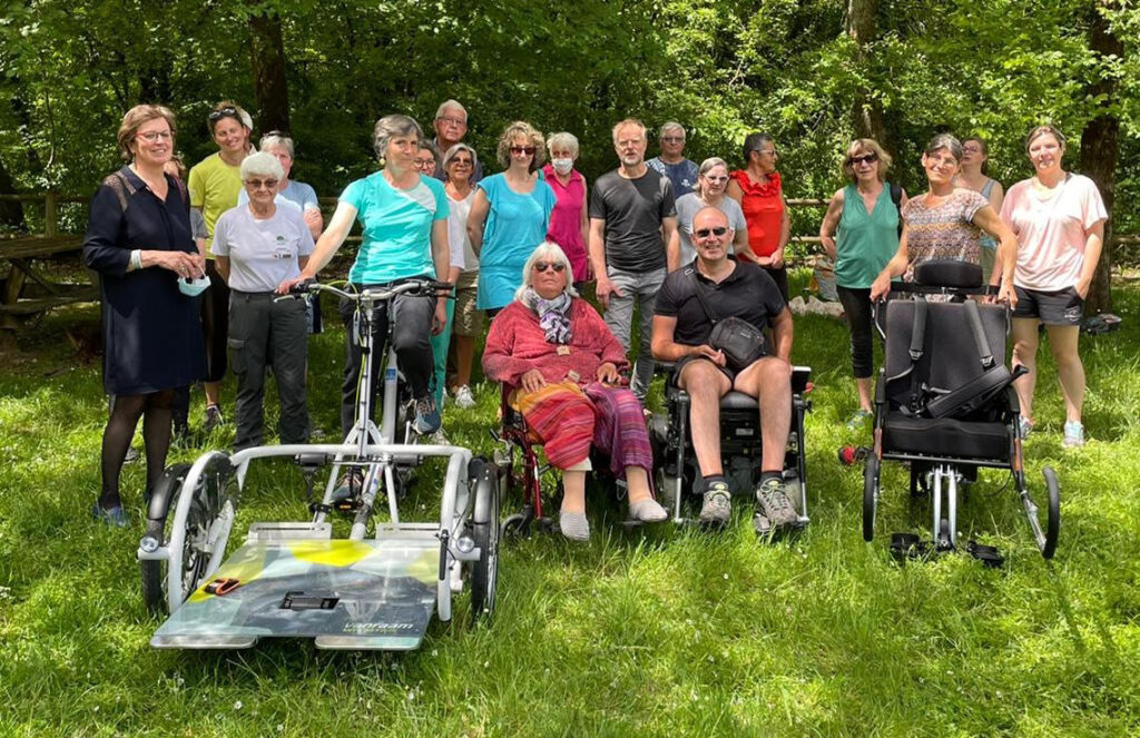 Des personnes valides et des personnes à mobilité réduite font une randonnée à l'aide de joëlettes et d'un vélo fauteuil.