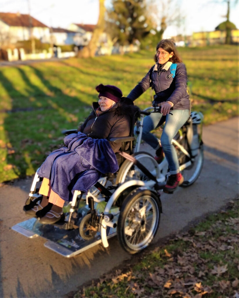 Une personne valide et une personne à mobilité réduite font une randonnée semi-urbaine à l'aide d'un vélo fauteuil.